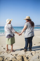 Großmutter und erwachsene Enkelin halten sich am Strand an einem sonnigen Tag an den Händen - RAEF000594