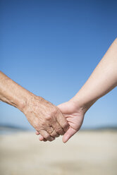 Elderly woman and young woman holding hands on the beach - RAEF000597