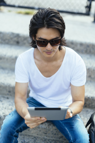 Mann sitzt auf einer Treppe und benutzt ein digitales Tablet, lizenzfreies Stockfoto