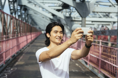 USA, New York City, Mann auf der Williamsburg Bridge in Brooklyn, der ein Selfie macht, lizenzfreies Stockfoto