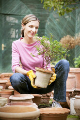 Smiling woman looking at potted plant in garden - RMAF000158