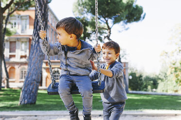 Junge schiebt seinen Bruder auf einer Schaukel auf dem Spielplatz - EBSF001003