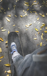 Boy standing on skateboard on path with autumn leaves - DEGF000568