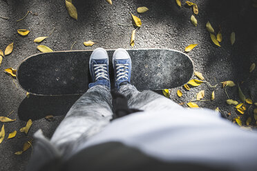 Boy standing on skateboard on path with autumn leaves - DEGF000569