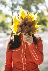 Woman covering her face with autumn leaves - DEGF000570