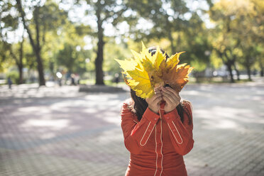 Frau bedeckt ihr Gesicht mit Herbstblättern - DEGF000571