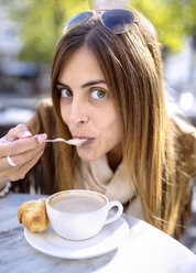 Spanien, Gijon, Junge Frau sitzt im Straßencafé und schlürft Cappuccino - MGOF000974