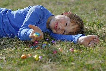 Lächelnder Junge auf einer Wiese mit vielen Schokoladeneiern liegend - LBF001275