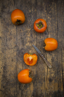 Whole and sliced kaki persimmons and a kitchen knife on wood - LVF004103