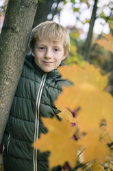 Porträt eines lächelnden Jungen, der sich im Herbst an einen Baumstamm lehnt - SARF002259