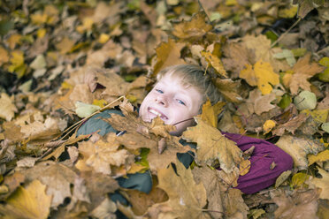 Porträt eines lächelnden Jungen, der auf dem mit Herbstblättern bedeckten Boden liegt - SARF002261
