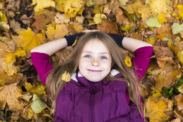 Portrait of smiling girl relaxing on autumn leaves on the ground - SARF002264