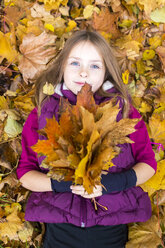 Porträt eines auf dem Boden liegenden Mädchens, das ein Bündel Herbstblätter hält - SARF002265