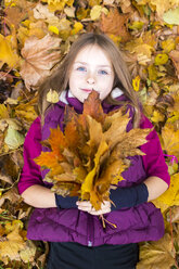 Portrait of girl lying on the ground holding bunch of autumn leaves - SARF002265