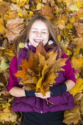 Porträt eines lachenden Mädchens, das auf dem Boden liegt und einen Strauß Herbstblätter hält - SARF002266