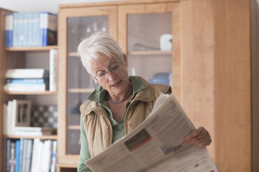 Porträt einer weißhaarigen älteren Frau, die zu Hause Zeitung liest - SGF001937