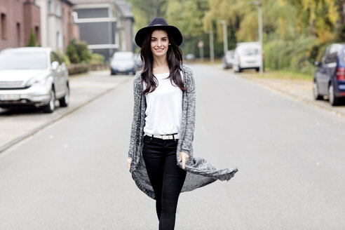 Porträt einer lächelnden jungen Frau mit schwarzem Hut, die auf einer Straße geht - GDF000888