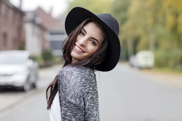 Portrait of smiling young woman wearing black hat looking over her shoulder - GDF000889