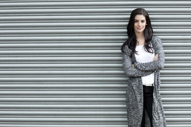 Portrait of young woman with crossed arms standing in front of roller shutter - GDF000890