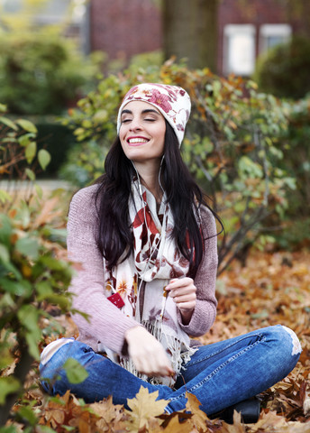 Porträt einer jungen Frau in Herbstmode, die mit Kopfhörern Musik hört, lizenzfreies Stockfoto