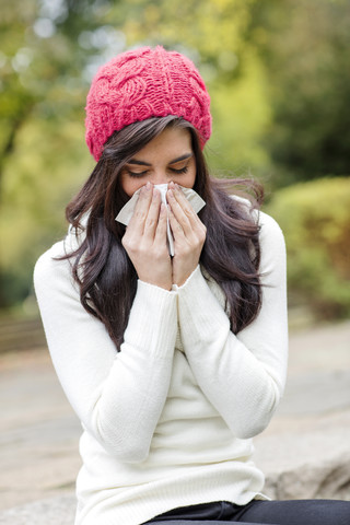 Young woman wearing red woolly hat blowing her nose stock photo