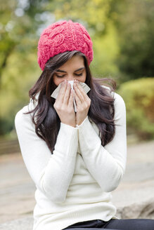 Young woman wearing red woolly hat blowing her nose - GDF000897