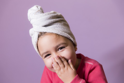Portrait of laughing little girl covering mouth with her hands wearing towel turban stock photo