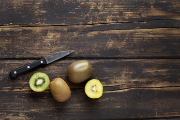 Ganze und in Scheiben geschnittene verschiedene Kiwis und ein Messer auf dunklem Holz - CSF026631