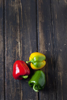 Rote, gelbe und grüne Paprika auf dunklem Holz - CSF026633
