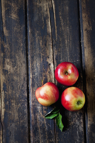 Drei rote Äpfel und Blätter auf dunklem Holz, lizenzfreies Stockfoto