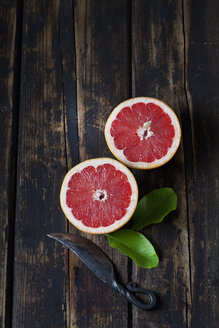 Aufgeschnittene rote Grapefruit, Blätter und Messer auf dunklem Holz - CSF026675