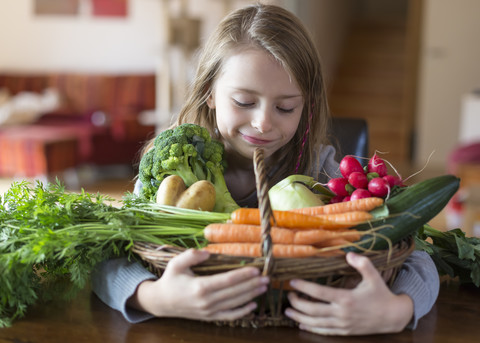 Porträt eines lächelnden Mädchens mit Weidenkorb mit frischem Gemüse zu Hause, lizenzfreies Stockfoto