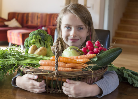 Porträt eines lächelnden Mädchens mit Weidenkorb mit frischem Gemüse zu Hause, lizenzfreies Stockfoto
