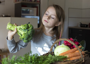 Porträt eines Mädchens mit einem Weidenkorb mit frischem Gemüse, das Brokkoli betrachtet - SARF002284