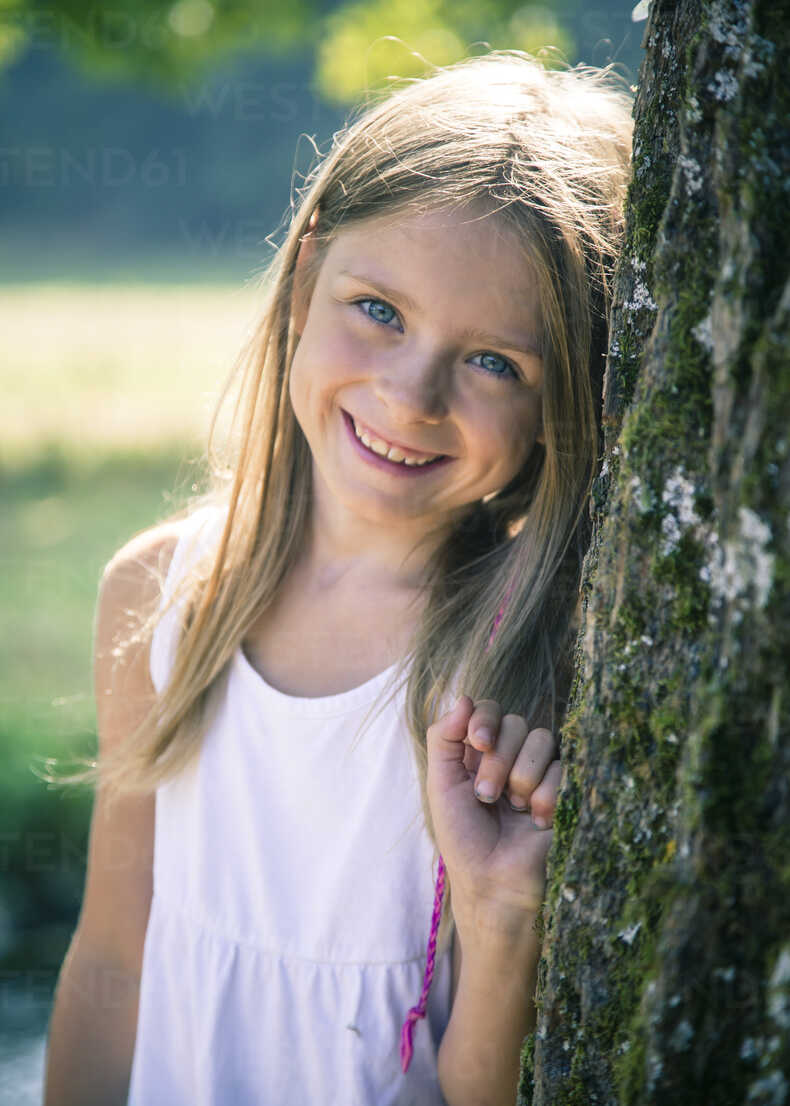 Portrait Of Smiling Little Girl Leaning Against Tree Trunk Stock Photo