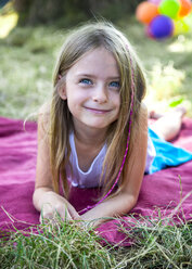 Portrait of smiling little girl lying on blanket on a meadow - SARF002290