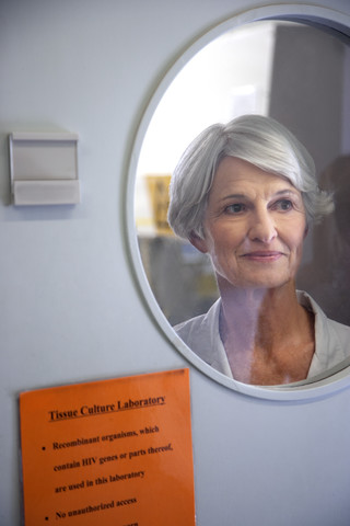 Ältere Frau schaut durch das Fenster der Labortür, lizenzfreies Stockfoto