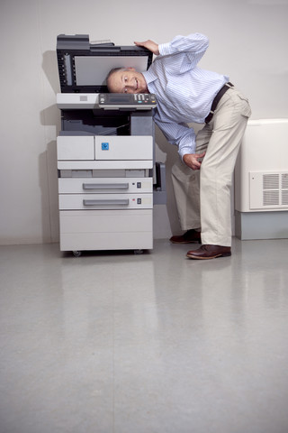 Senior man putting head in copying machine stock photo