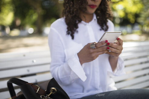 Junge Frau sitzt auf einer Parkbank und benutzt ihr Smartphone, Nahaufnahme - RAEF000616