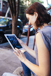 USA, New York City, smiling woman sitting on stairs using digital tablet - GIOF000383