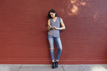 Portrait of woman with digital tablet leaning against red brick wall - GIOF000384