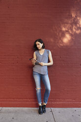 Porträt einer Frau mit digitalem Tablet, die sich gegen eine rote Backsteinmauer lehnt - GIOF000385