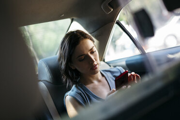 Porträt einer jungen Frau, die in einem Taxi sitzt und ihr Smartphone benutzt - GIOF000405