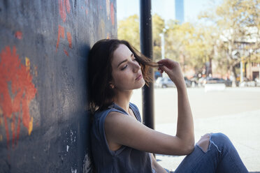 USA, New York City, daydreaming young woman sitting on the ground leaning against a wall - GIOF000416