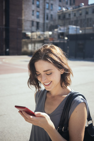 USA, New York City, Manhattan, lächelnde junge Frau schaut auf ihr Smartphone, lizenzfreies Stockfoto