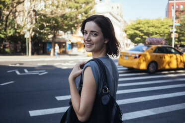 USA, New York City, Manhattan, Porträt einer lächelnden jungen Frau beim Überqueren einer Straße - GIOF000420