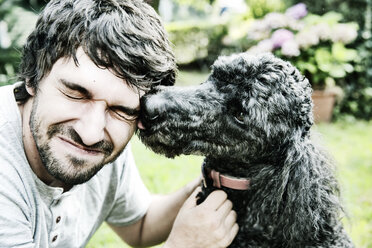 Poodle licking the face of his owner in the garden - JATF000758