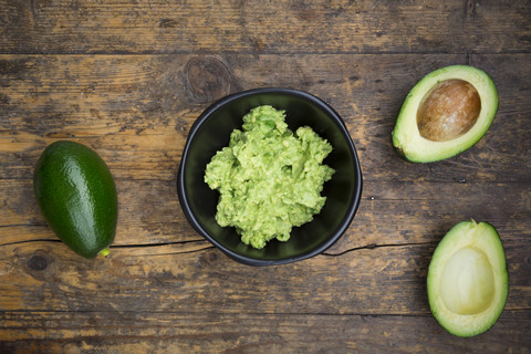 Schale mit Guacamole und ganzen und geschnittenen Avocados auf dunklem Holz, lizenzfreies Stockfoto