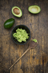 Bowl of Guacamole, cooking spoon and whole and sliced avocados on dark wood - LVF004105