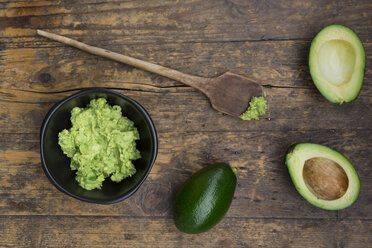 Bowl of Guacamole, cooking spoon and whole and sliced avocados on dark wood - LVF004106